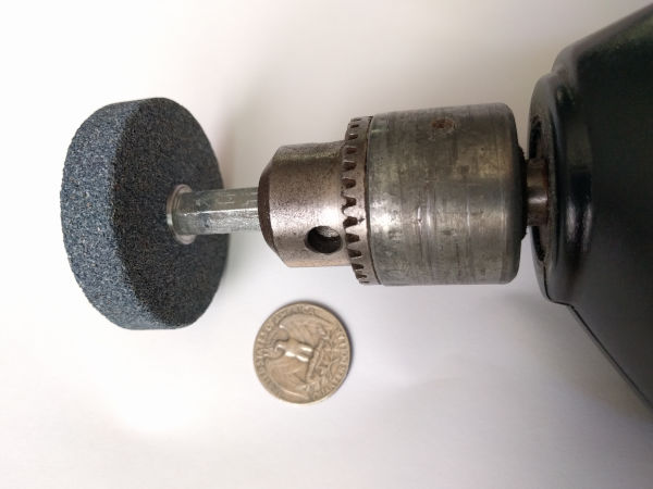 A grinding wheel in the chuck of a drill and a US Quarter coin