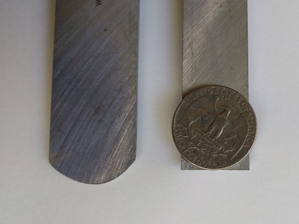 The underside of two chisels. One has a round edge. The other has a flat edge and a US Quarter coin atop it just touching the edge.