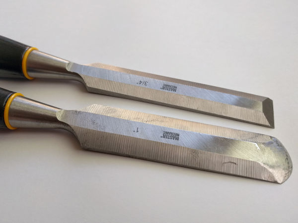 Two chisels. The three-quarter-inch chisel has a flat cutting edge. The one-inch chisel has a rounded cutting edge.
